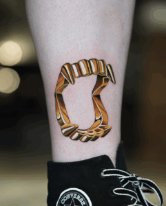 Tattoo of a stylized, three-dimensional golden chain link on a leg, showcasing intricate details and shading, relevant to Pony Lawson's artistic style at Inked Tattoo Studios.